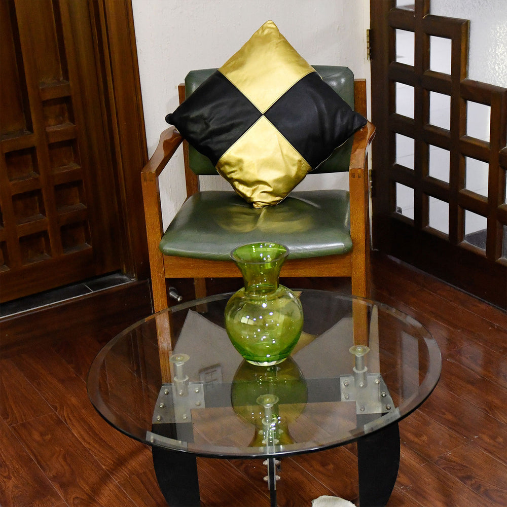 Green vase on a glass table with a chair and decorative pillow in the background.

