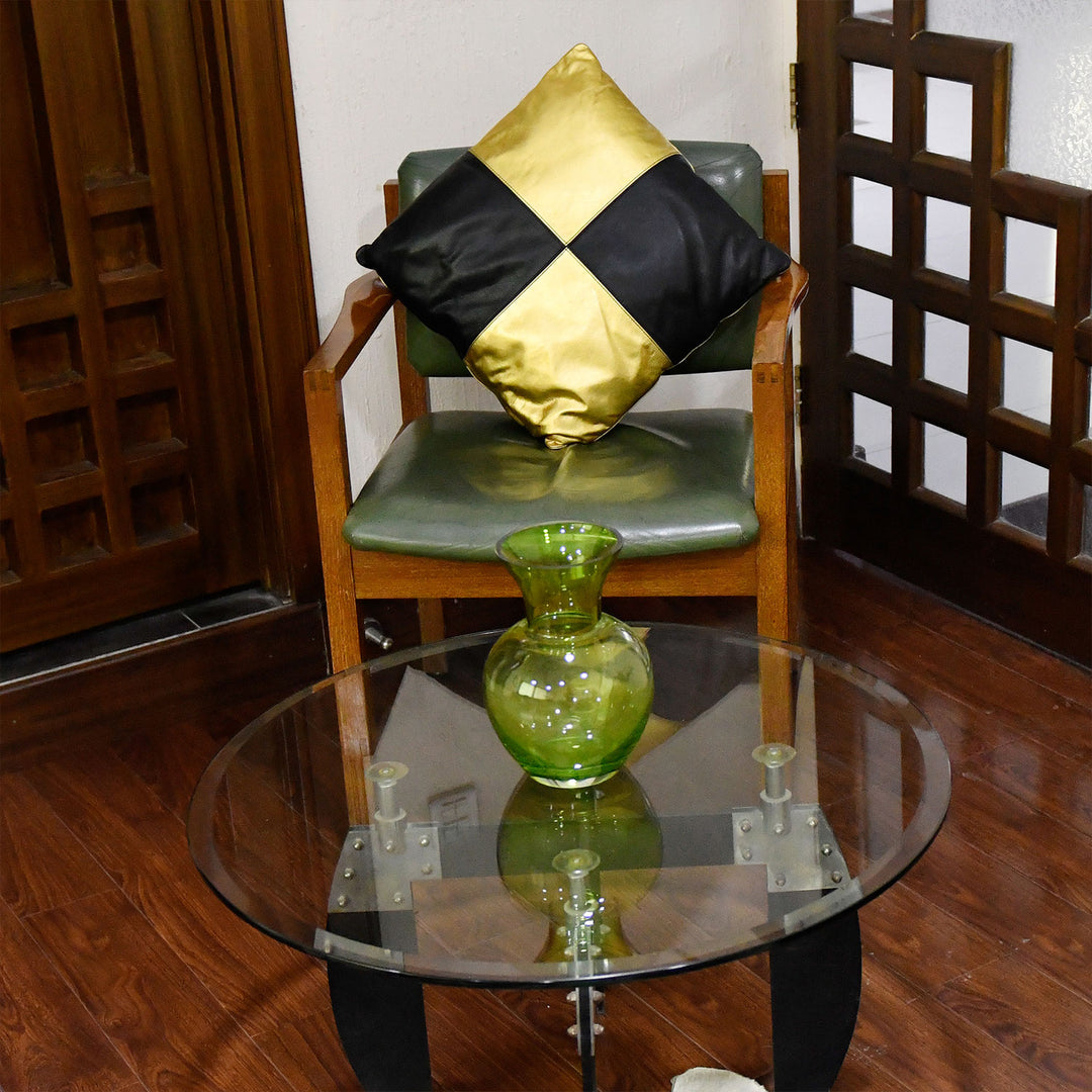 Green vase on a glass table with a chair and decorative pillow in the background.

