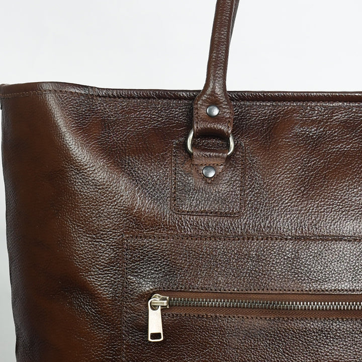 Close-up of a brown leather bag with metal zippers and studs on a light gray background