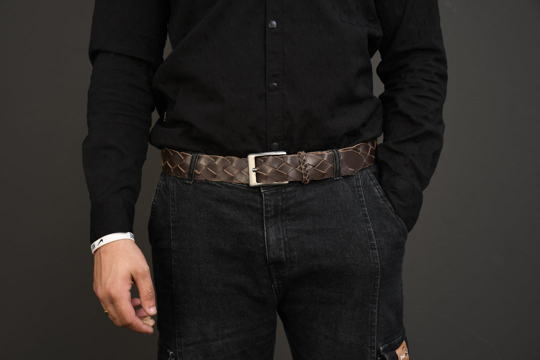 Person wearing a black shirt and dark jeans with a brown belt on a gray background