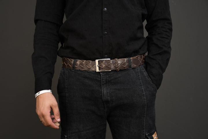 Person wearing a black shirt and dark jeans with a brown belt on a gray background