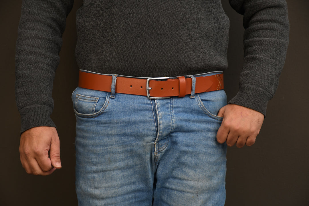 Person wearing a brown belt, gray sweater, and blue jeans against a dark background