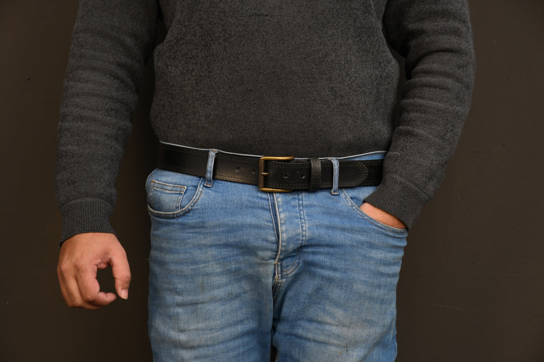 Person wearing a dark gray sweater and blue jeans with a black belt on a brown background