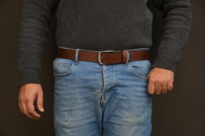 Person wearing a dark gray sweater and blue jeans with a brown belt against a dark background