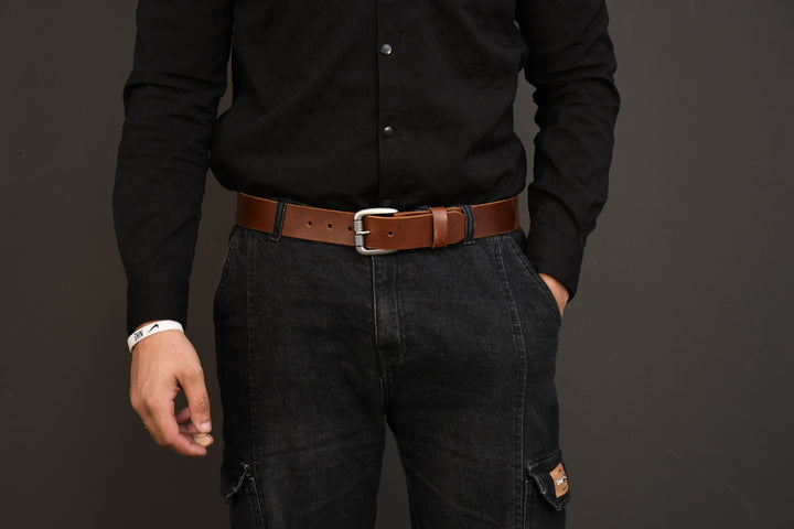 Person wearing a black shirt, dark jeans, and a brown belt against a gray background