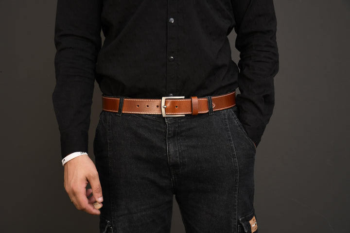 Person wearing a black shirt and dark jeans with a brown belt on a gray background