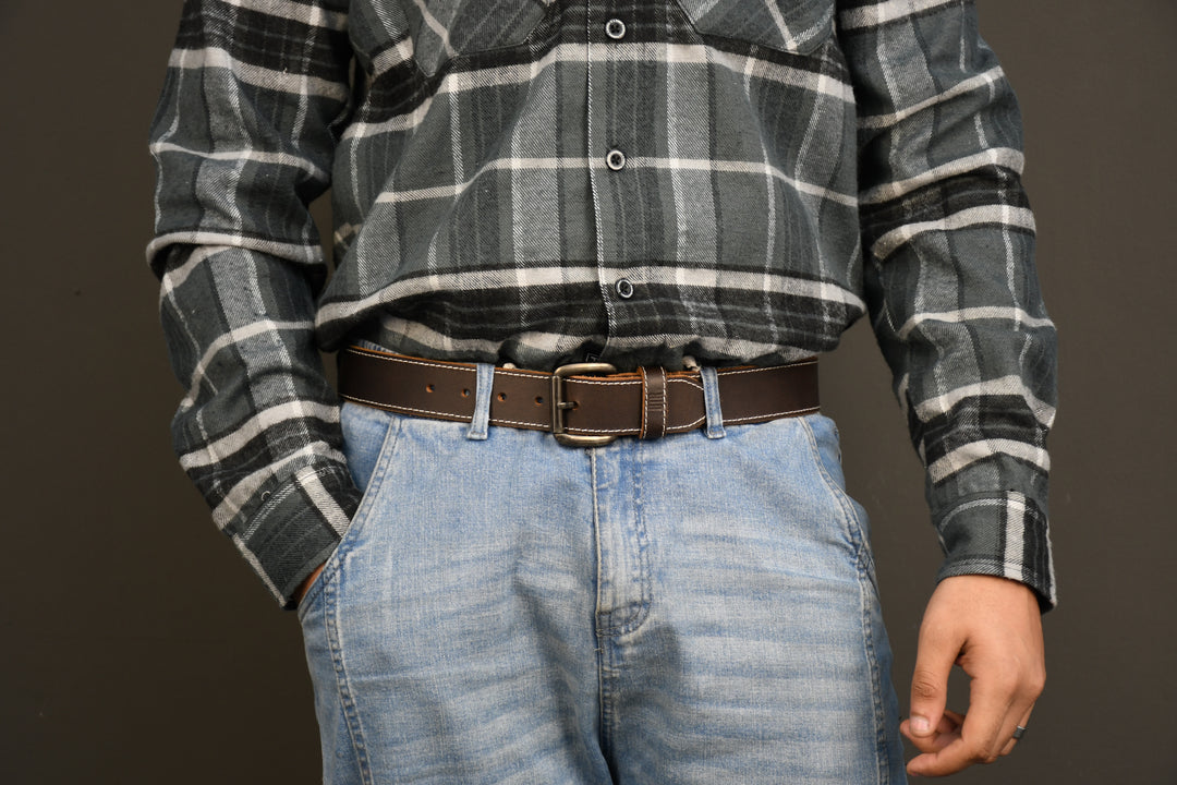 Person wearing a plaid shirt and jeans with a brown belt on a dark background