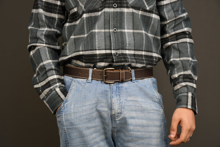 Person wearing a plaid shirt and jeans with a brown belt on a dark background