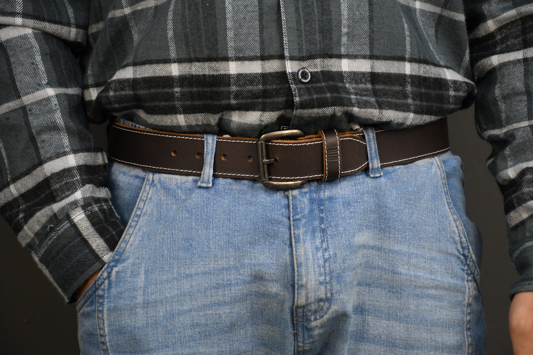 Person wearing a plaid shirt, jeans, and a brown belt with a dark background