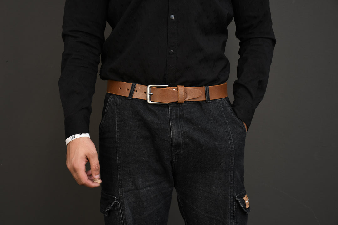 Person wearing a black shirt, dark jeans, and a brown belt on a gray background