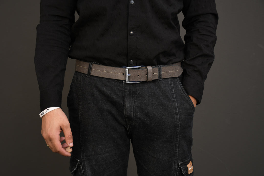 Person wearing a black shirt and dark pants with a Taupe grey belt on a gray background