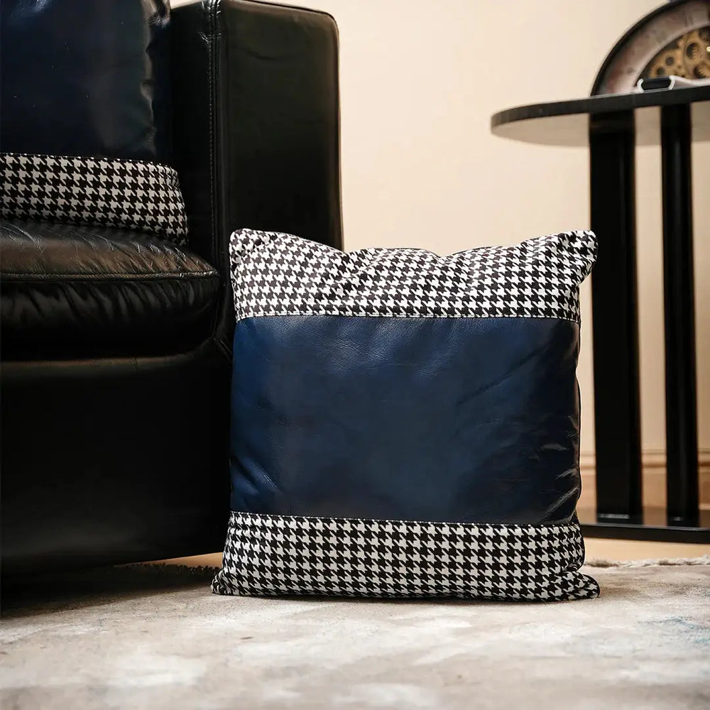Houndstooth-patterned pillow on a wooden floor with a black leather chair and table in the background.