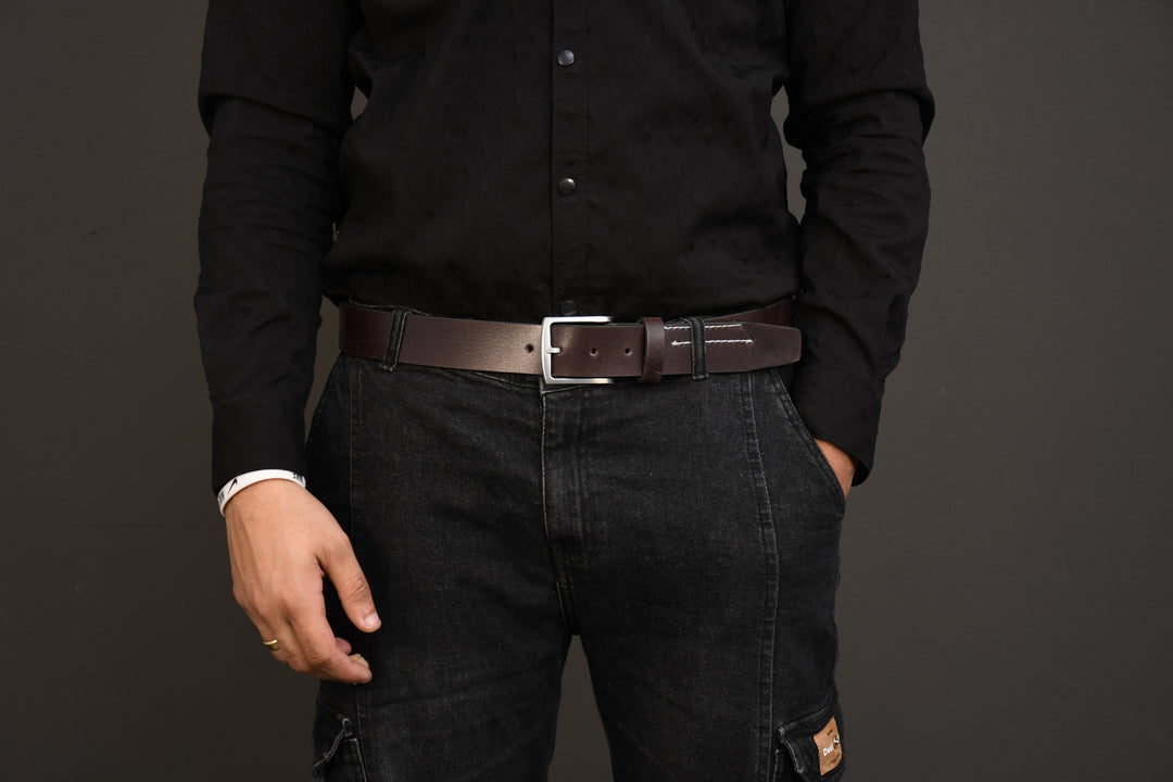Person wearing a black shirt and dark jeans with a brown belt on a gray background