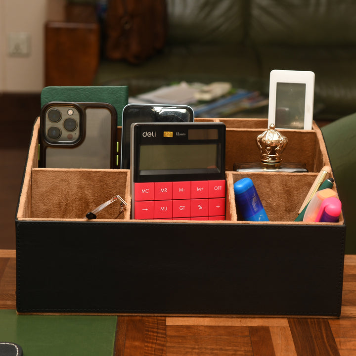 Leather organizer with office supplies including a phone, calculator, and markers on a wooden surface.