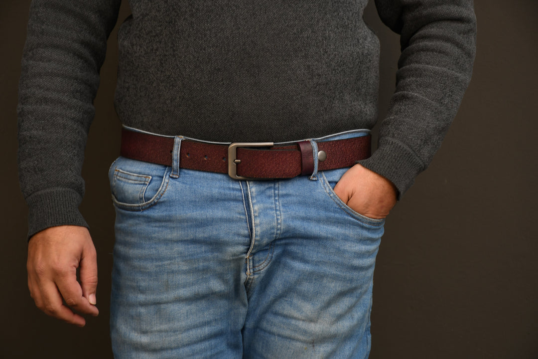 Person wearing a dark gray sweater and blue jeans with a brown belt on a dark background