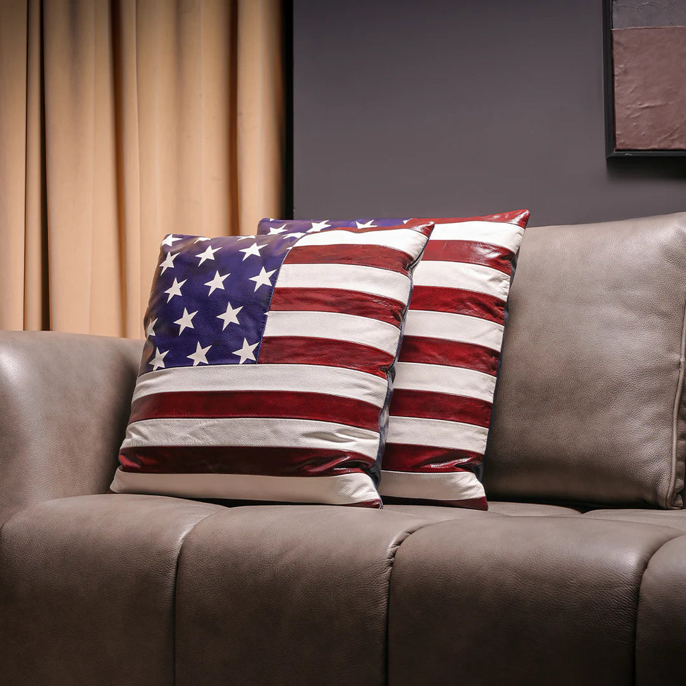 Two American flag patterned pillows on a brown sofa with a neutral background