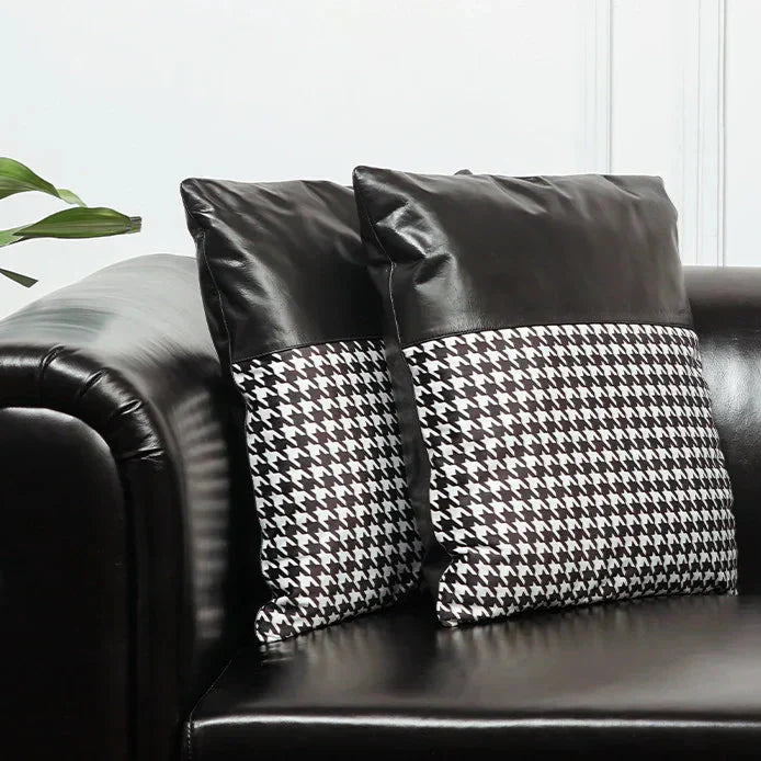 Black leather sofa with houndstooth patterned cushions against a white wall.