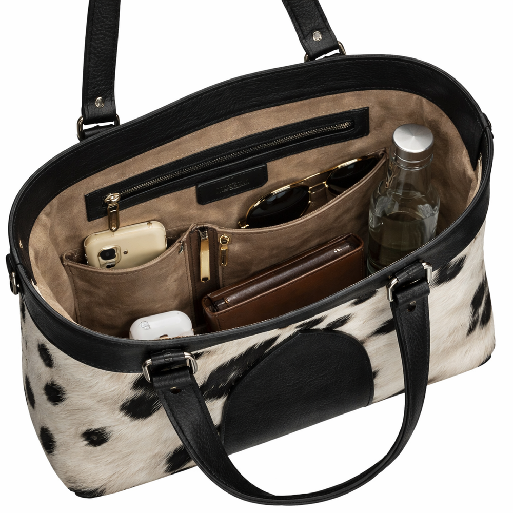 Cow print handbag with black handles and interior compartments.